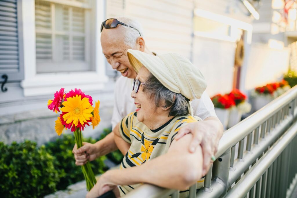 an elderly couple laughs and holds a bouquet of flowers